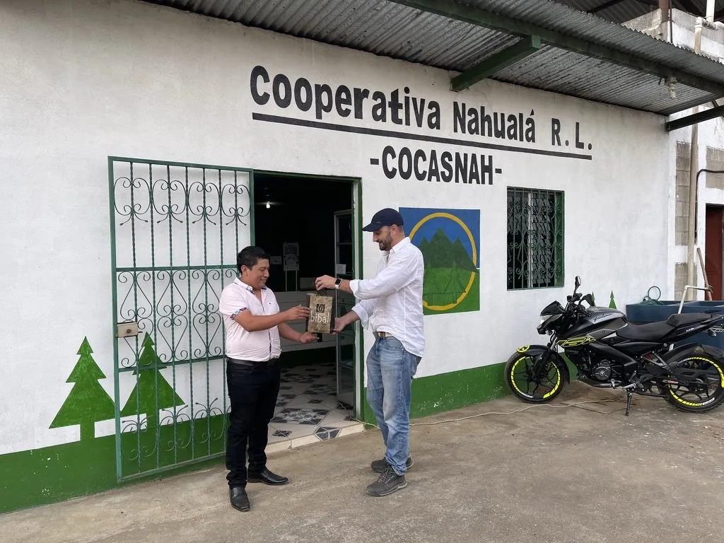 Thomas Bertrand remet un sachet de café Bibal à un responsable de la Cooperativa Nahualá R.L. (COCASNAH), devant l'entrée de la coopérative