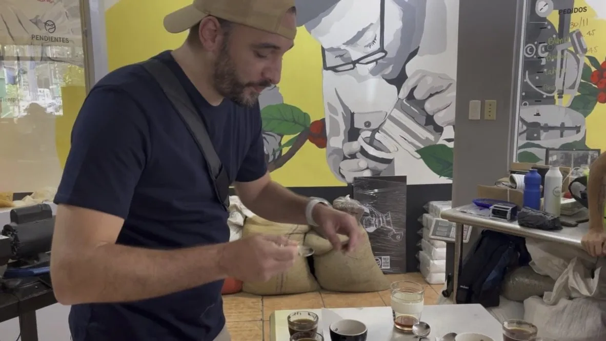 Thomas Bertrand, cuillère de cupping à la main, goûte des cafés devant une fresque murale représentant un dégustateur
