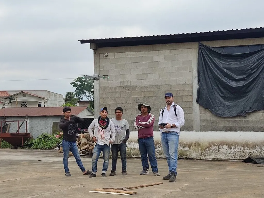 Thomas Bertrand pilote un drone devant le bâtiment de la coopérative, entouré de quatre travailleurs qui regardent l'appareil décoller