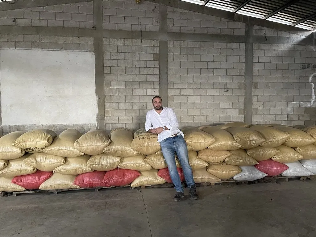 Thomas Bertrand appuyé sur des sacs de café vert empilés dans un entrepôt