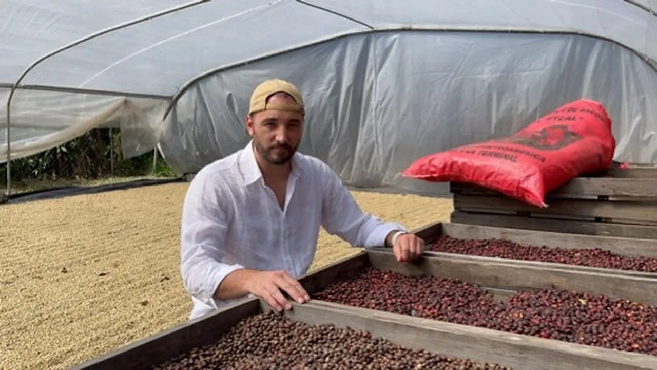 Thomas Bertrand devant des lits de séchage sous serre : cerises séchant entières au premier plan, café en parche derrière
