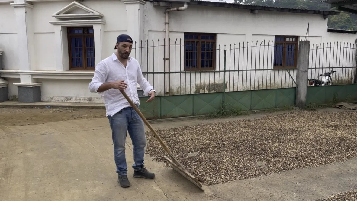 Thomas Bertrand ratisse le café en parche qui sèche sur un patio, devant le bâtiment de la coopérative