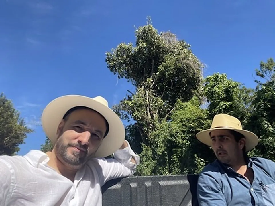 Deux membres de l'équipe en chapeaux de paille à l'arrière d'un pick-up, sous les arbres