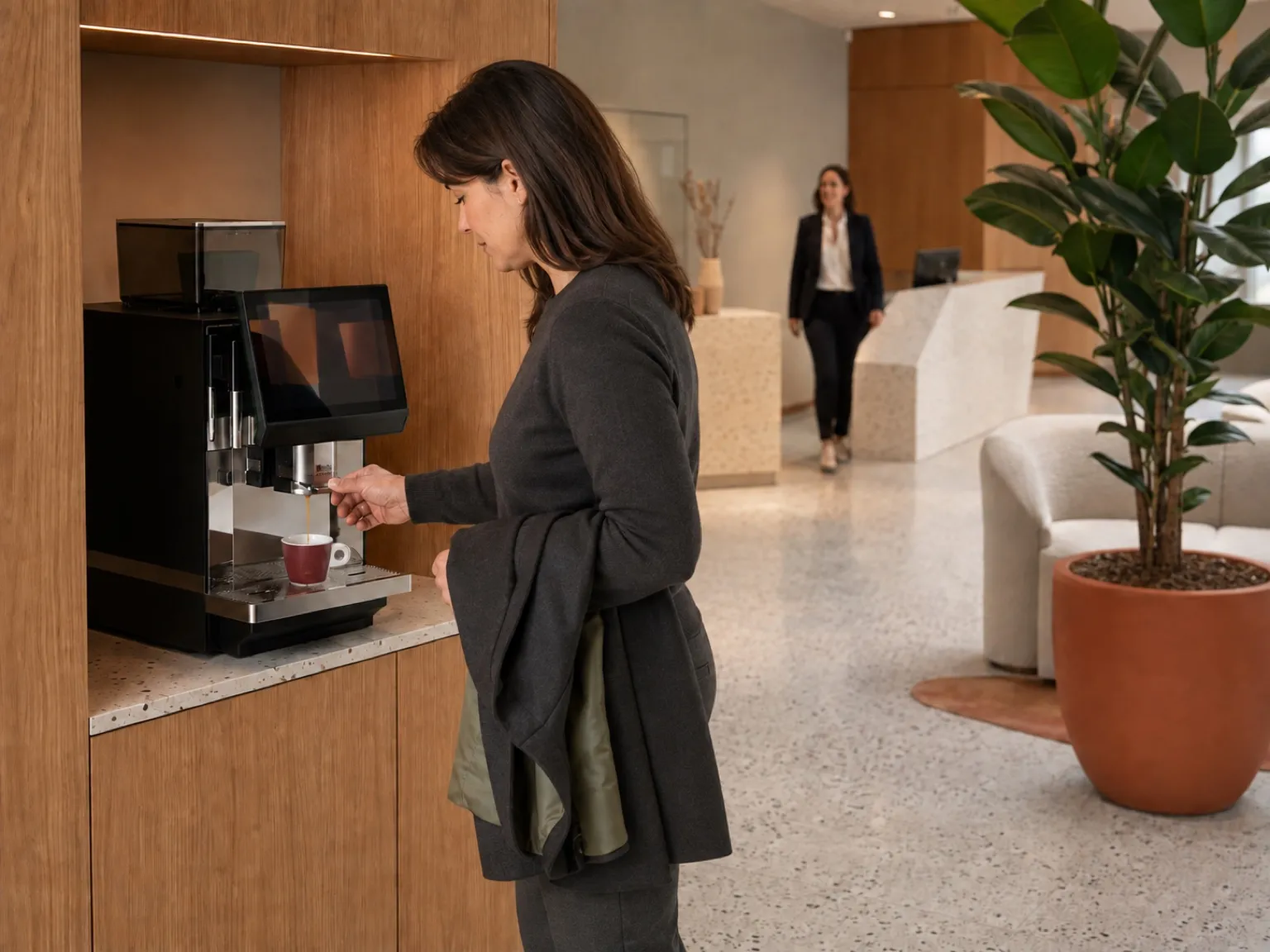 Hall d'accueil d'entreprise : une visiteuse se sert un café à l'espace café pendant qu'on vient la chercher