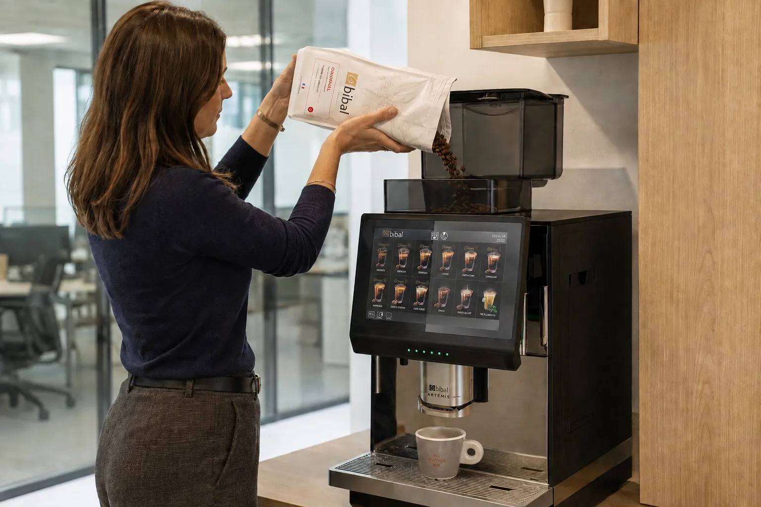 Une collaboratrice remplit le bac à grains de la machine Artémis avec un paquet de café Bibal dans l'espace Coffee Lounge