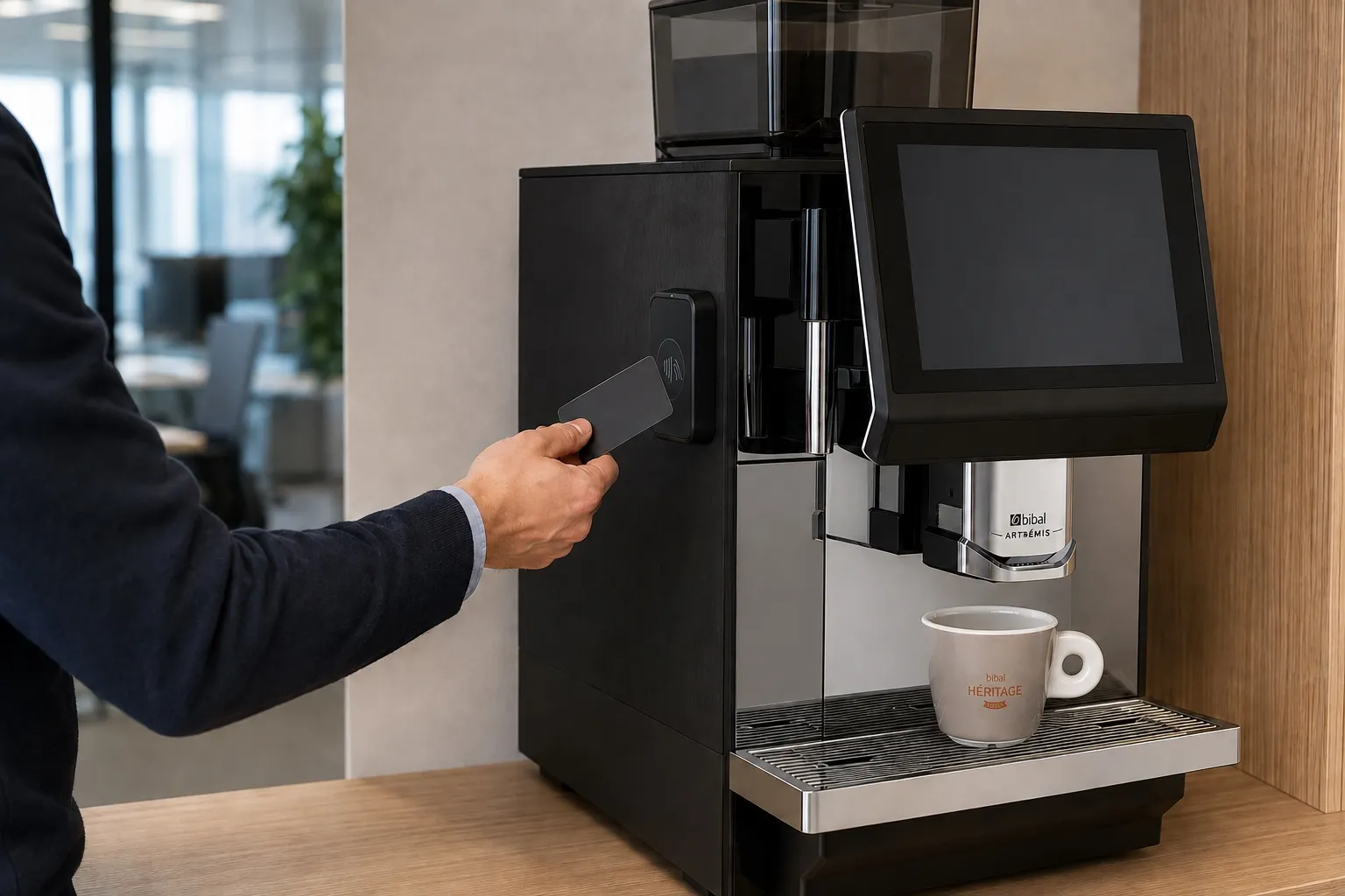 Un collaborateur approche une carte bancaire unie du lecteur sans contact de la machine automatique, tasse Héritage déjà en place sous le bec
