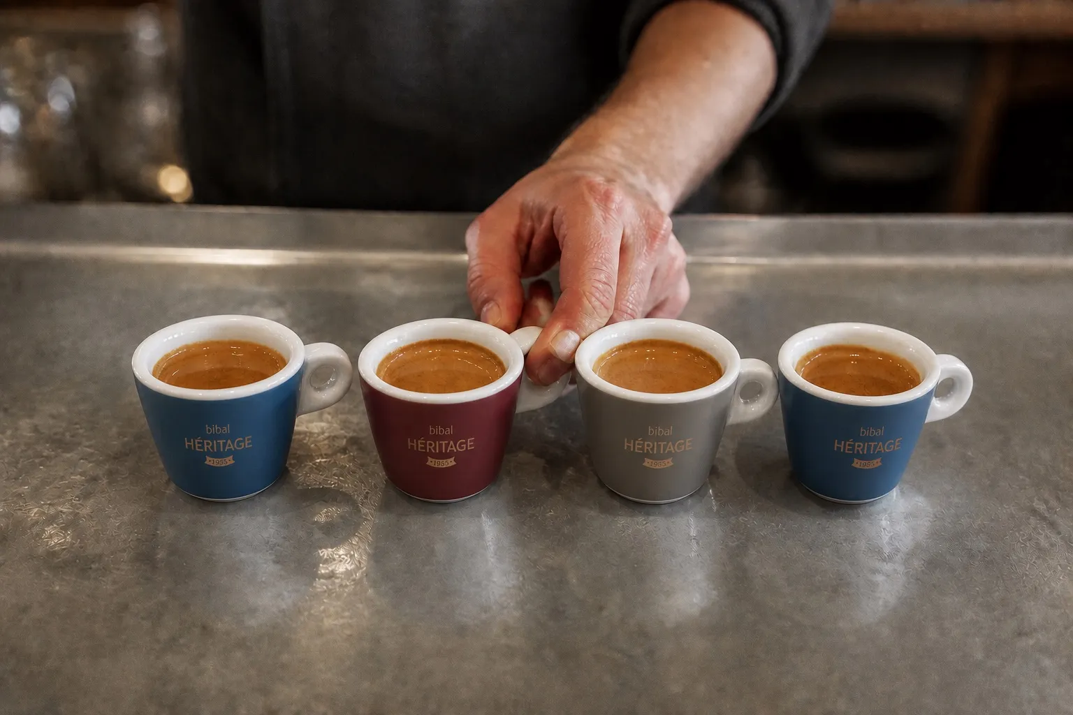 Petites tasses d’expresso à la crema tigrée alignées sur le zinc, la main du serveur en saisit deux