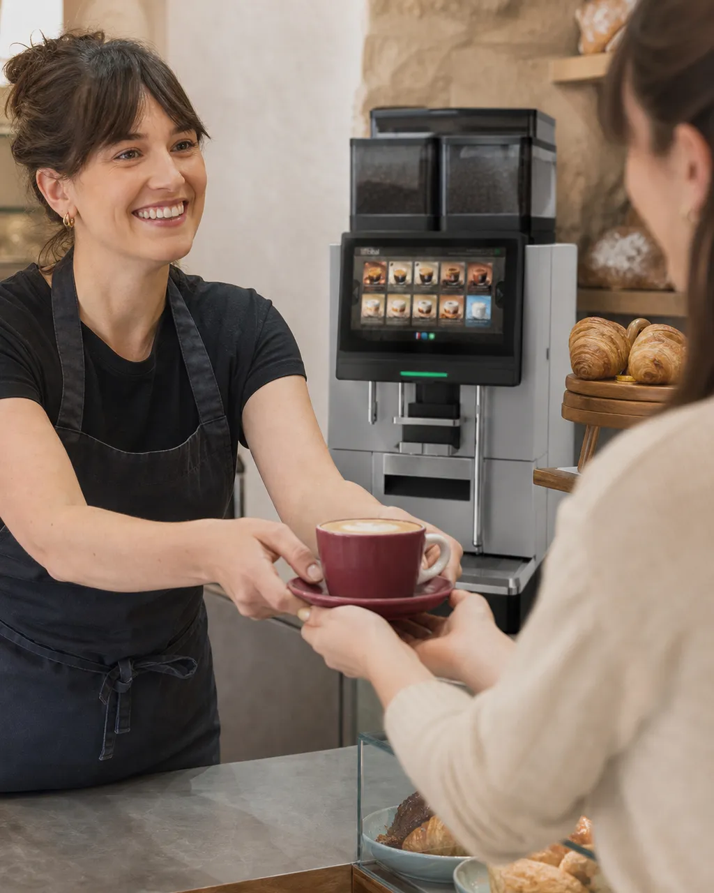 Vendeuse servant un cappuccino Héritage au comptoir devant la machine Astra